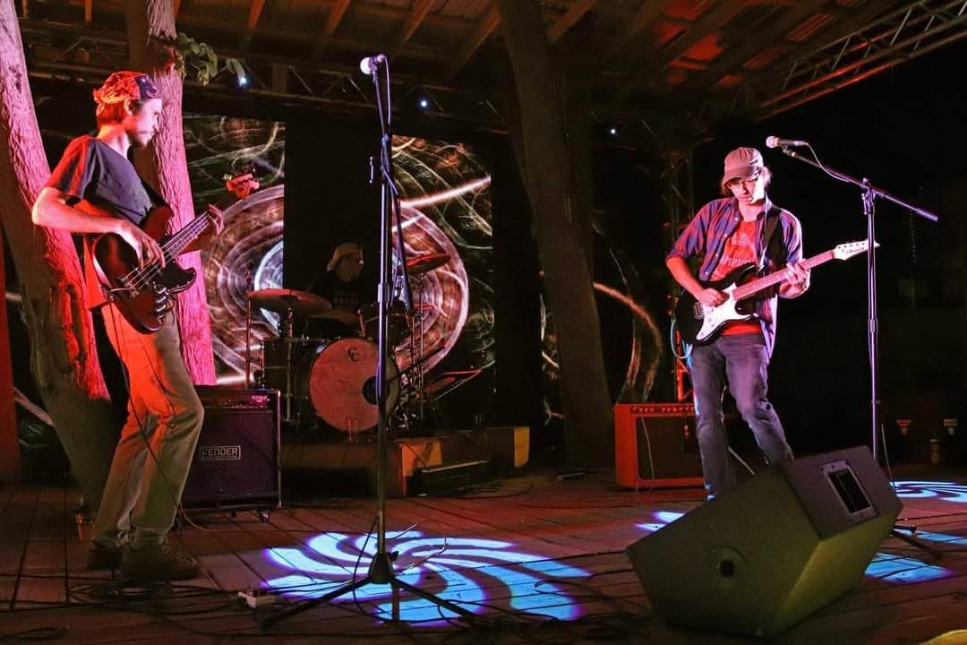 Trio performing outdoors under colored stage lighting